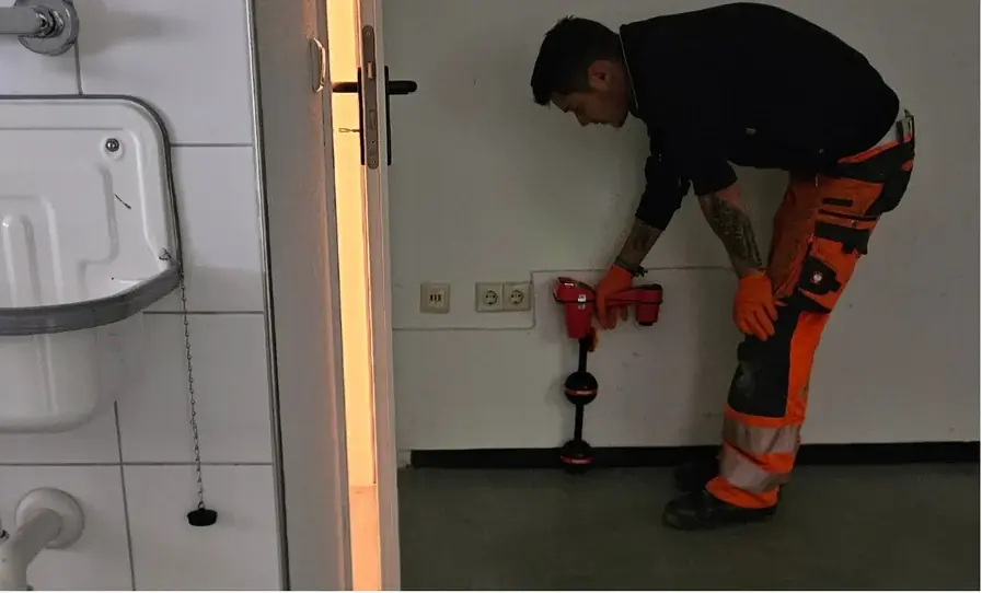 Mitarbeiter mit Ortungsgerät an einer Wand im Gebäude